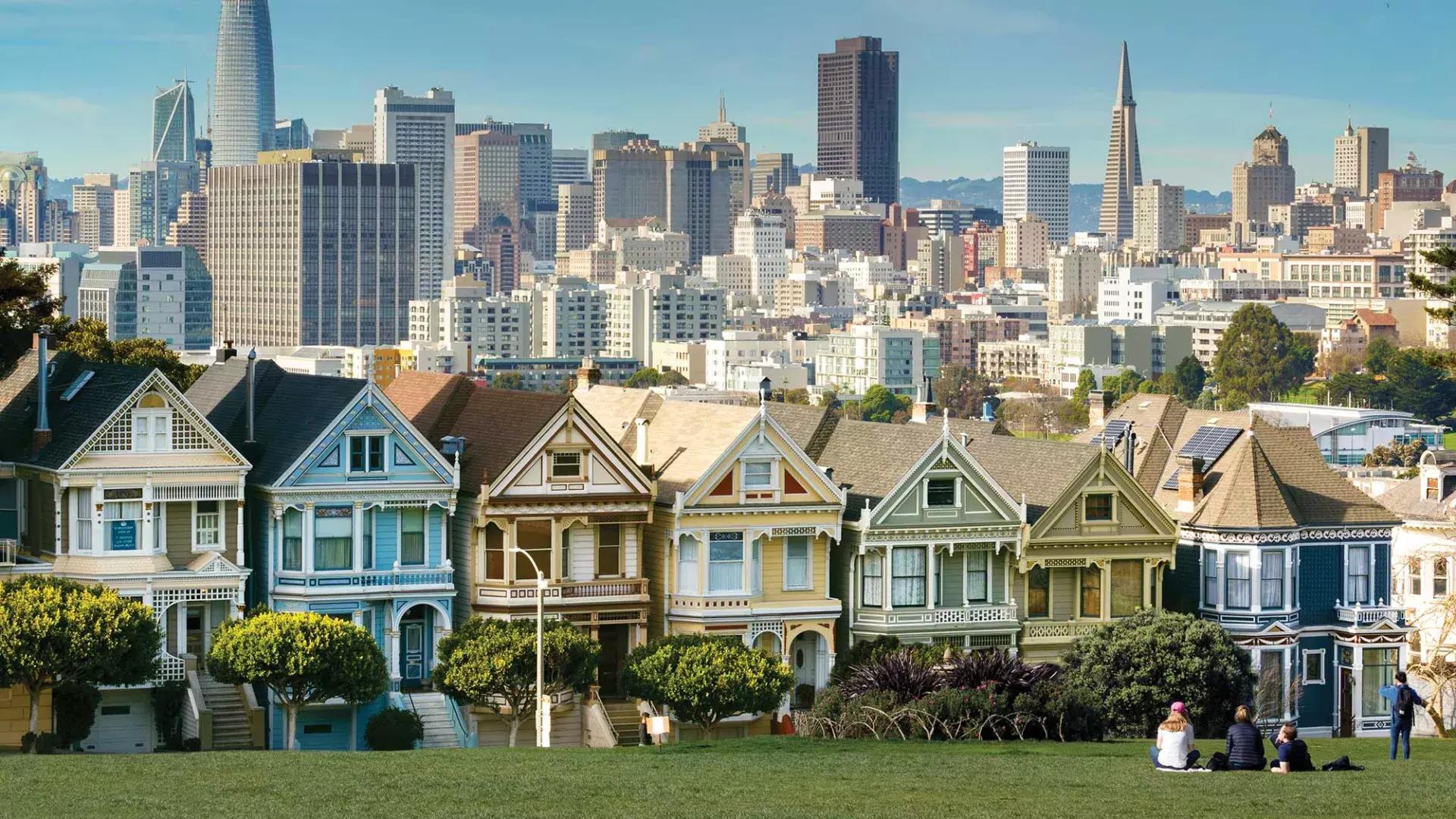 Les pique-niqueurs sont assis sur l'herbe du parc Alamo Square, avec les Painted Ladies et les toits de San Francisco en arrière-plan.